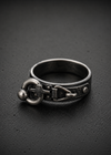 A silver-toned metal ring with a gothic knot and cross motif, resting on a dark textured surface.