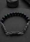 A beaded bracelet with glossy black round beads and textured silver-toned metal chain details, displayed on a dark slate surface.