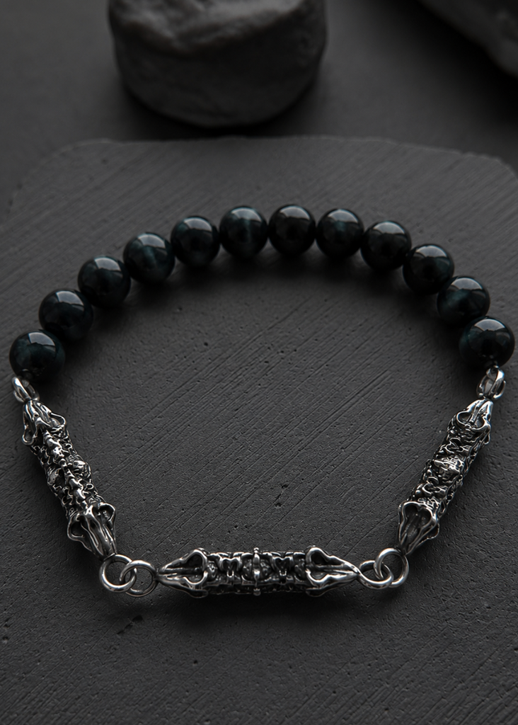 A beaded bracelet with glossy black round beads and textured silver-toned metal chain details, displayed on a dark slate surface.