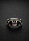 A silver ring featuring a textured winged design on the band and a central round pink gemstone, displayed on a dark textured background.