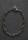 A silver-toned chain bracelet with oval links, each featuring a small amber-orange gemstone, displayed on a dark textured background.